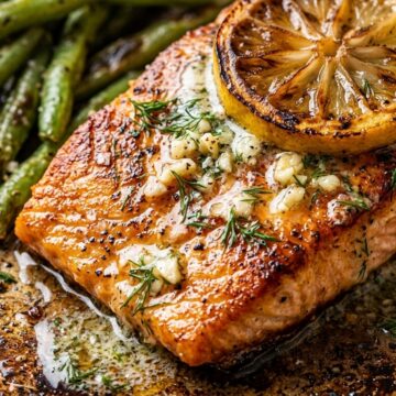 Ultra close-up macro of seared flaky salmon fillet topped with caramelized lemon slice, garlic herb butter, and charred green beans