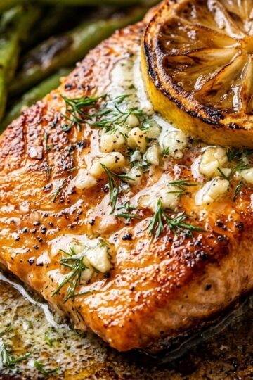 Ultra close-up macro of seared flaky salmon fillet topped with caramelized lemon slice, garlic herb butter, and charred green beans