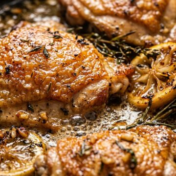 Ultra close-up macro of sizzling crispy lemon herb chicken thighs in garlic butter pan sauce