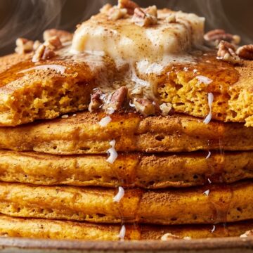 Towering stack of fluffy spiced sweet potato pancakes with melting cinnamon pecan butter and maple syrup