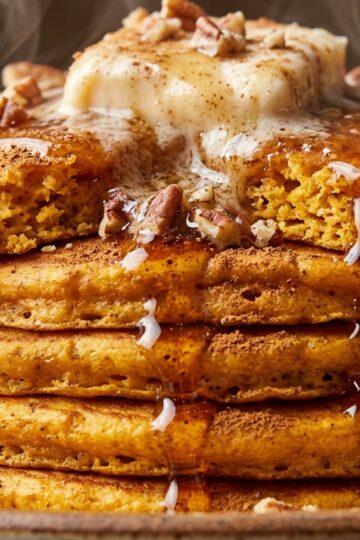 Towering stack of fluffy spiced sweet potato pancakes with melting cinnamon pecan butter and maple syrup