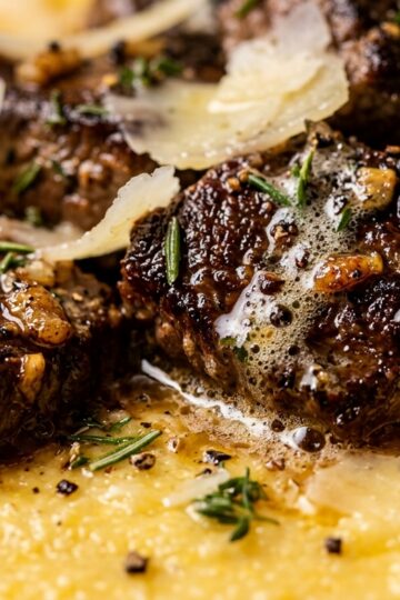 Ultra close-up macro of garlic butter steak bites over creamy parmesan polenta