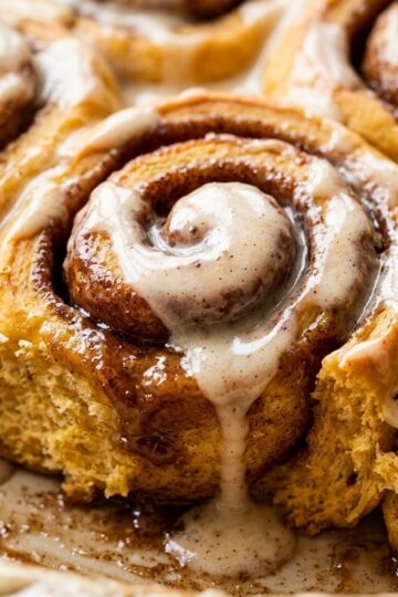 Ultra close-up macro texture of warm gooey pumpkin cinnamon rolls with melting maple cream glaze