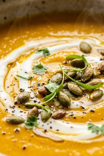 Ultra close-up macro texture of velvety spiced roasted pumpkin and coconut bisque with toasted pepitas